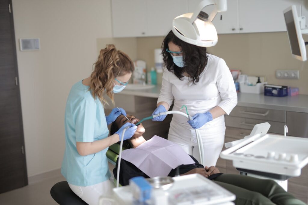 Young female dentist examining teeth of patient with assistant in modern clinic