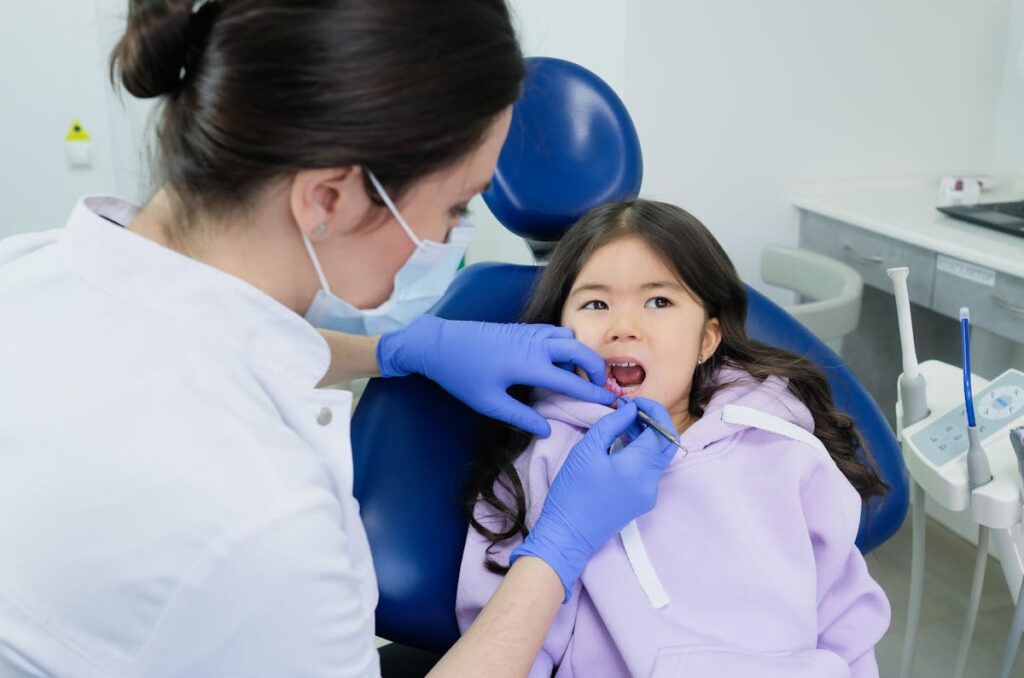 Woman in White Button Up Shirt Wearing Face Mask Cleaning the Girl's Teeth