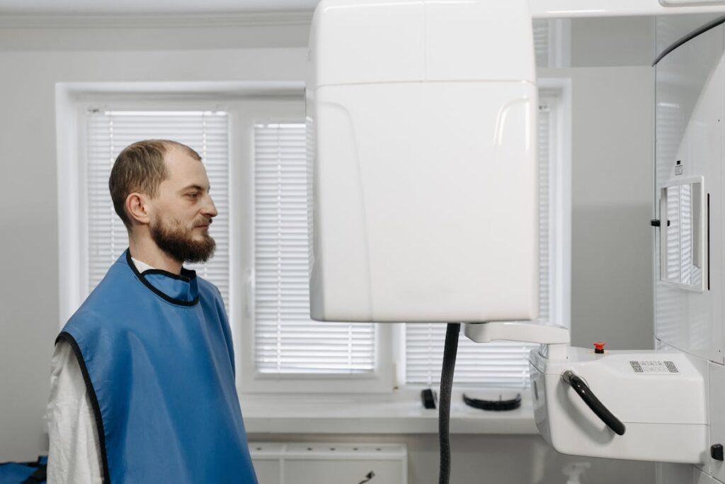A man in a medical gown receiving a dental x-ray examination in a clinical setting.