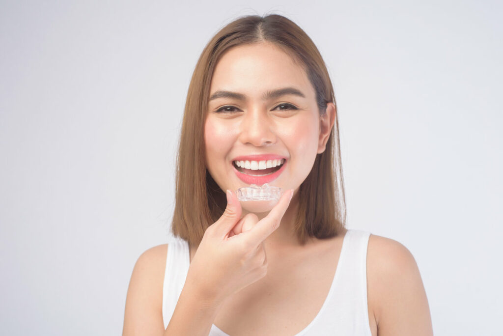 A young smiling woman holding invisalign braces over white background studio, dental healthcare and Orthodontic concept.