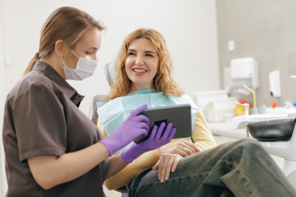 Doctor use tablet computer in stomatology. Young caucasian female at dental checkup with dentist in modern clinic.
