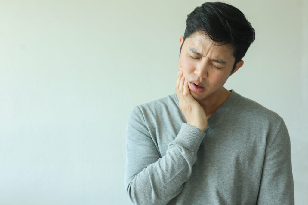 close up young asian man frown and use hand to massage on cheek after feeling pain or hurt from tmj muscle symptom at home for un healthy lifestyle and treatment concept