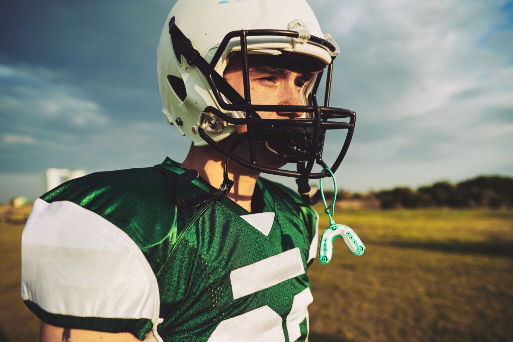 Young American football player taking a break with his mouth guard hanging from his helmet during a team practice session