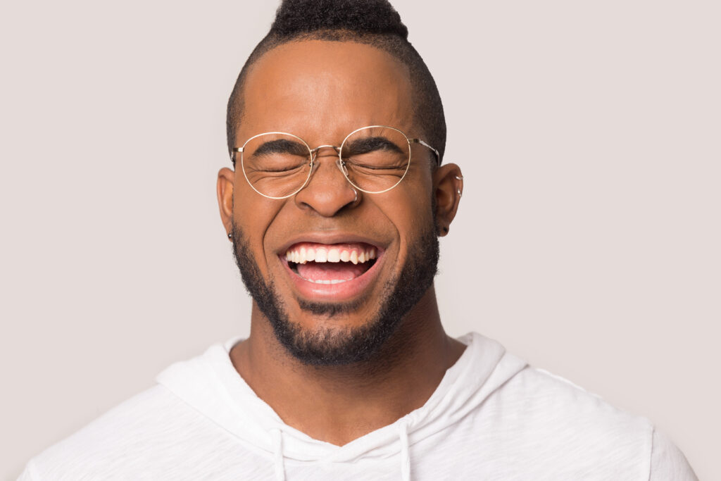 Funny African American man with wide healthy smile laughing at joke close up, happy male in glasses having fun, enjoy laughter, positive emotion, isolated on studio background copy space