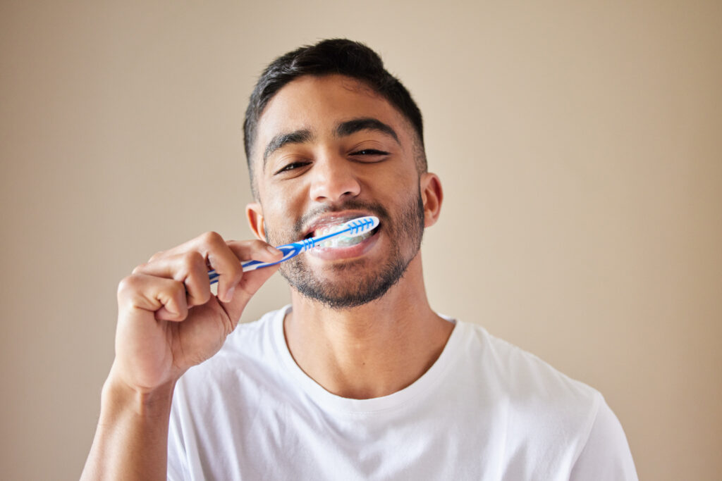 Studio shot of a handsome young man brushing his teeth against a studio background.